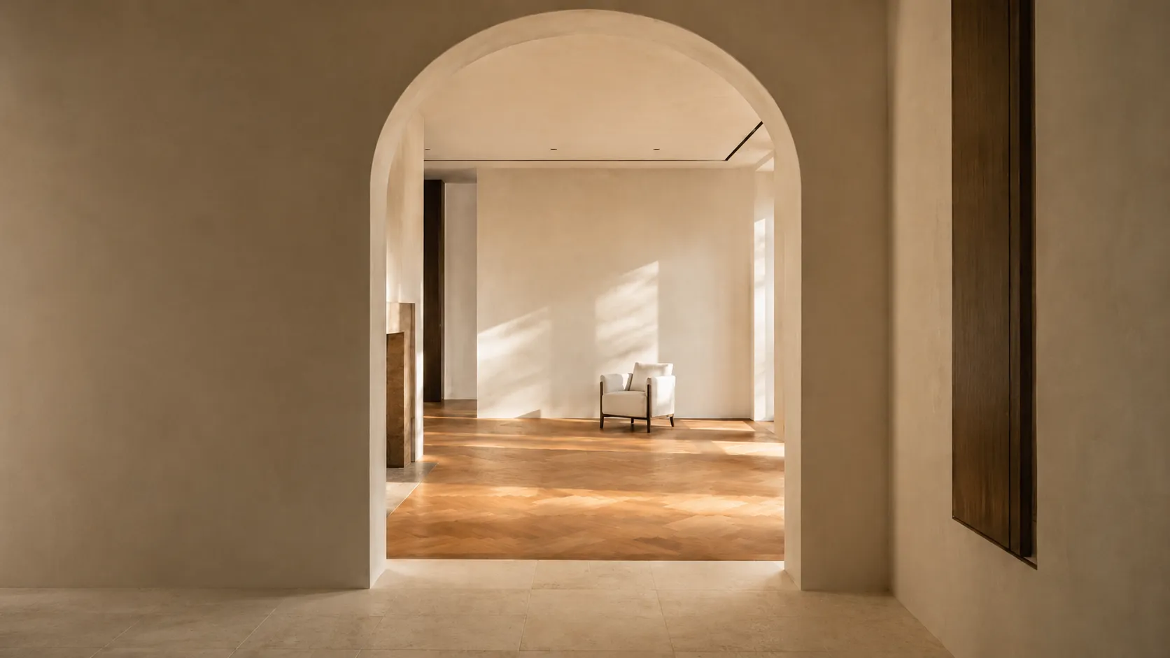 An arched limewashed doorway opening onto a sunlit drawing room with parquet floors and a single linen chair.