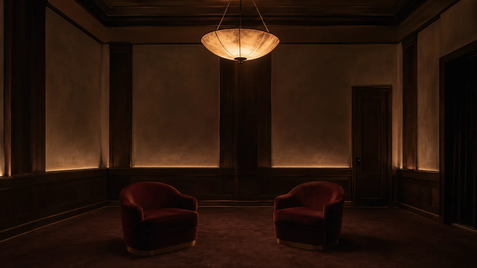 An empty private screening room with deep velvet chairs and a single amber pendant lamp casting warm light.